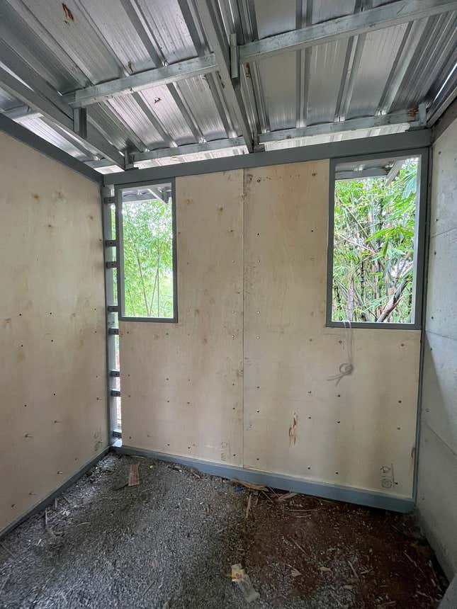 Φωτογραφία του εσωτερικού ενός μερικώς τελειωμένου δωματίου με τοίχους από κόντρα πλακέ και δάπεδο από σκυρόδεμα. 