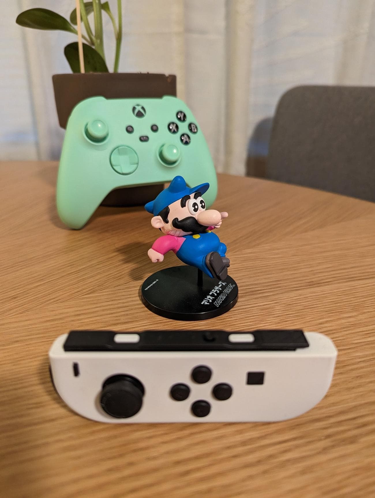 Μια φωτογραφία ενός ειδωλίου Super Mario και δύο χειριστηρίων παιχνιδιών, τραβηγμένη με zoom 1x.