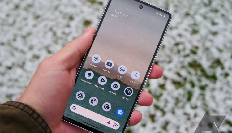 A person wearing a brown jacket holds a Google Pixel 7 with its screen illuminated.