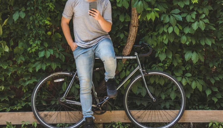 Man with bike resting against tree checks his messages. 