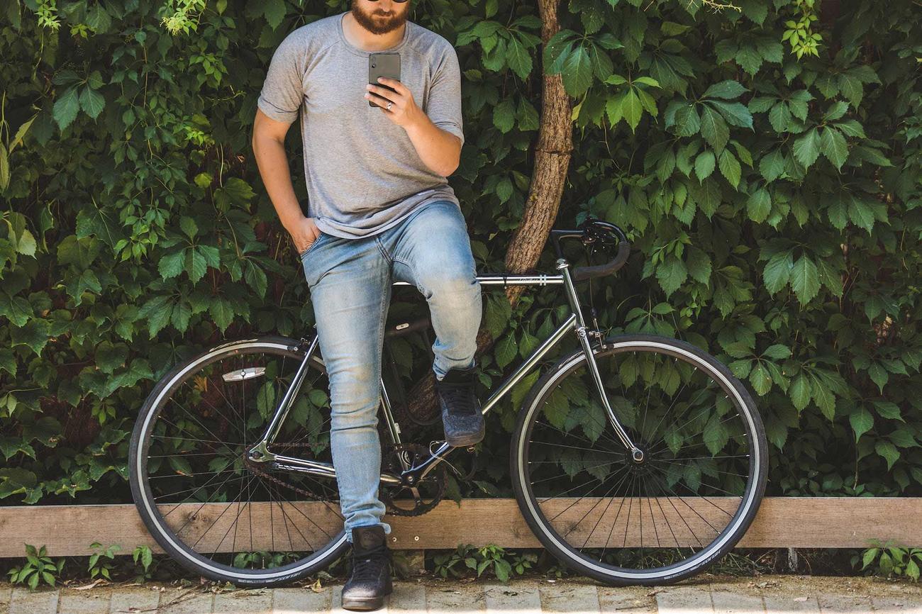 Man with bike resting against tree checks his messages. 
