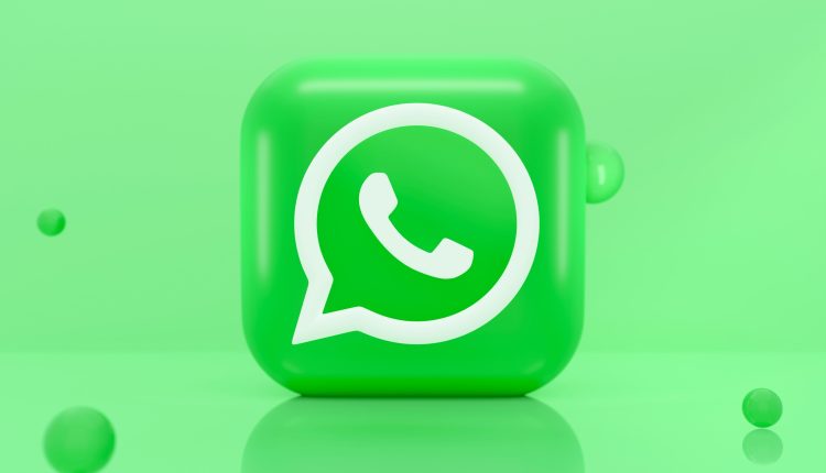 The front-facing WhatsApp logo is displayed on a three-dimensional green cube that sits on a solid green background. Dark green bubbles add visual interest to the image.