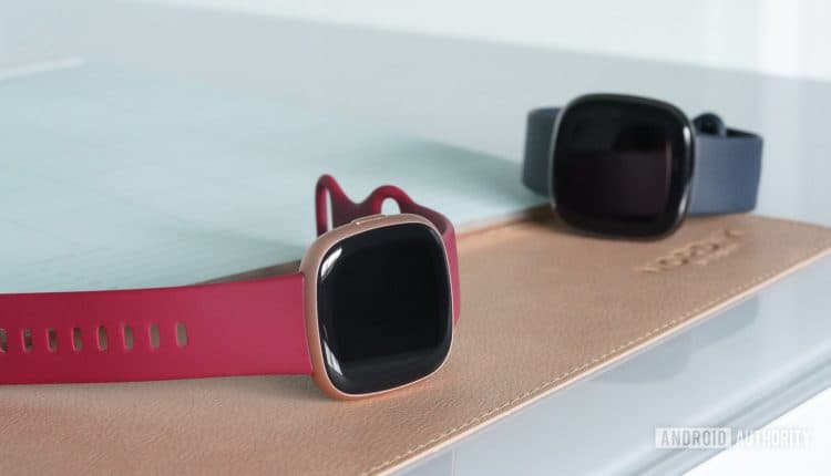 A Fitbit Versa 4 rests on a desk alongside a Fitbit Sense.