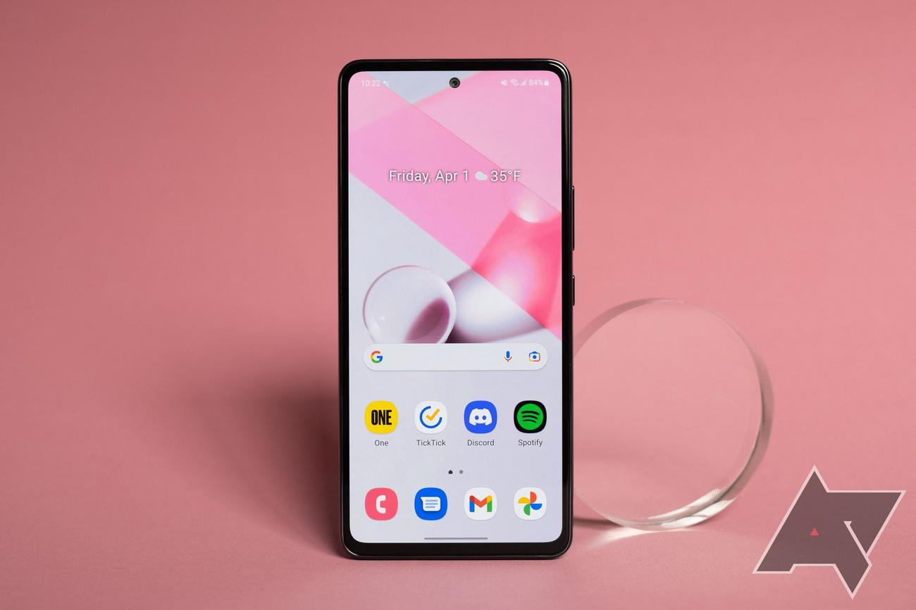 A smartphone with a pink and gray background sits against a pink backdrop. 