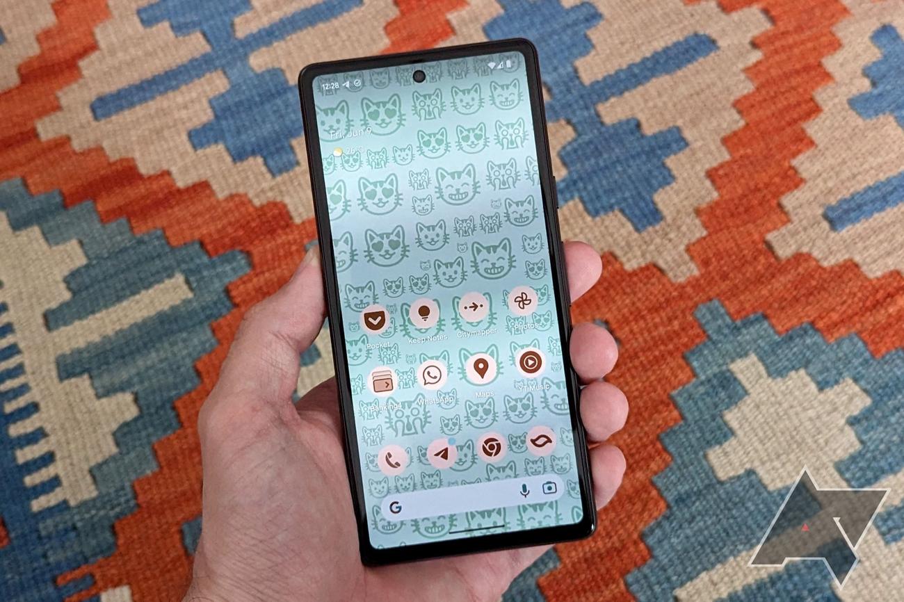 A Google Pixel 7a with a blue-ish cat emoji wallpaper on its home screen