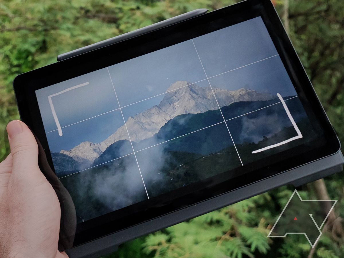 A hand holding a tablet showing an image of a mountain on the screen