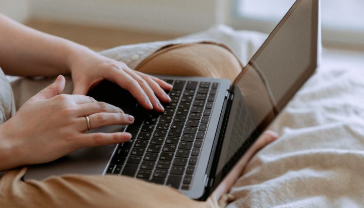 A cropped image of a person wearing camel pants with a laptop in their lap.