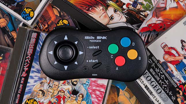 Ο ασύρματος ελεγκτής NEOGEO CD 8BitDo κάθεται πάνω σε ένα σωρό παιχνίδια CD NEOGEO στις κοσμηματοθήκες τους.