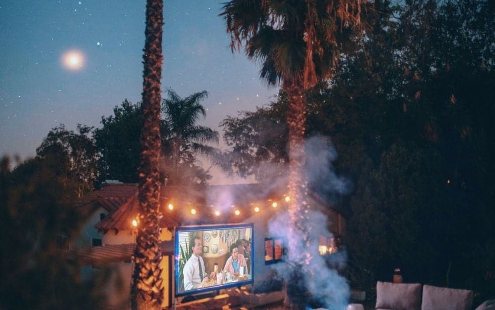 A film set with an outdoor projector with lights in the trees and the smoke of the burning fire.