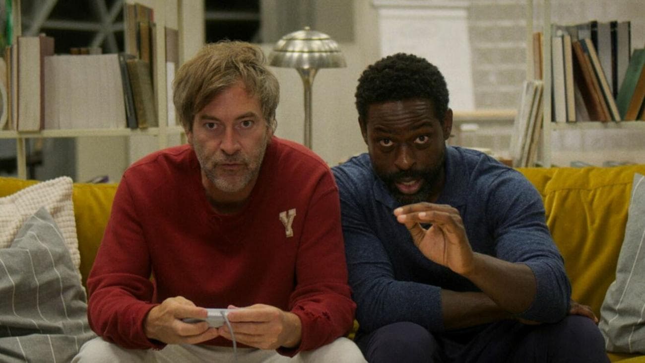 Δύο άντρες παίζουν βιντεοπαιχνίδια ενώ κάθονται σε έναν καναπέ. 