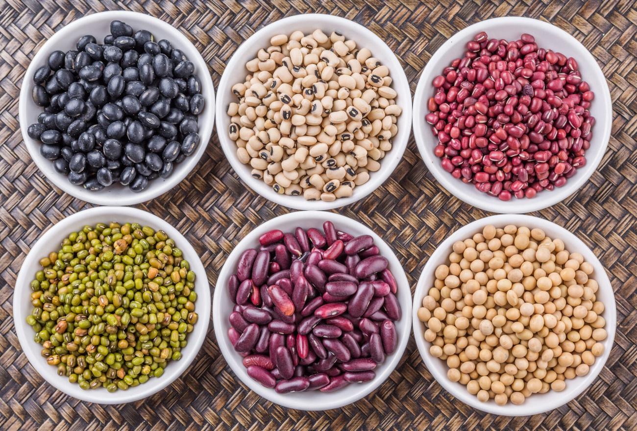 Black beans, white beans, kidney beans, green beans, pinto beans, and garbanzo beans arranged in bowls on a table for maximum daily fiber intake