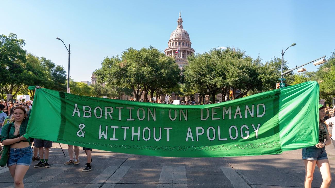 Abortion rights demonstrators march behind a sign that reads "Abortion on demand and without apology," near the State Capitol in Austin, Texas on June 25, 2022. Abortion rights defenders fanned out across America on June 25 for a second day of protest against the Supreme Court