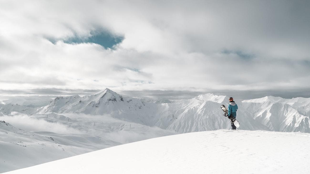 snowboarder on top of a snowy mountain holding a snowboard and wearing the best snowboarding jacket