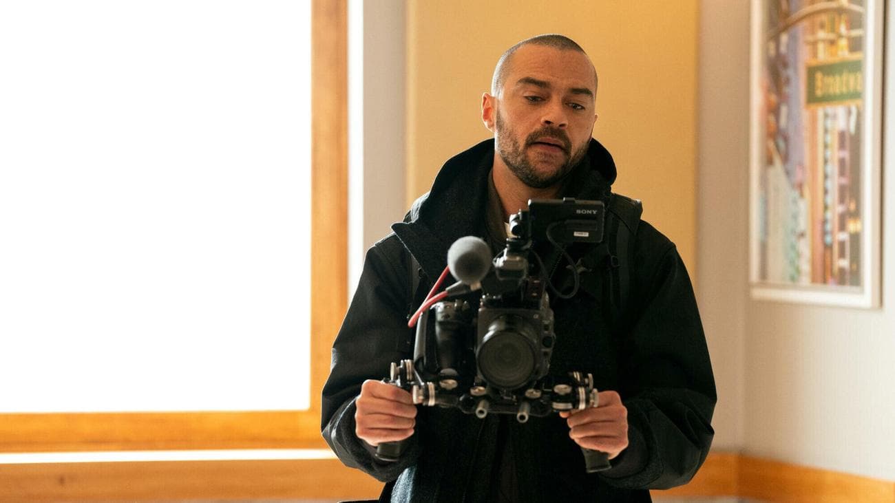 A young man wearing a black hoodie holds up a film camera. 