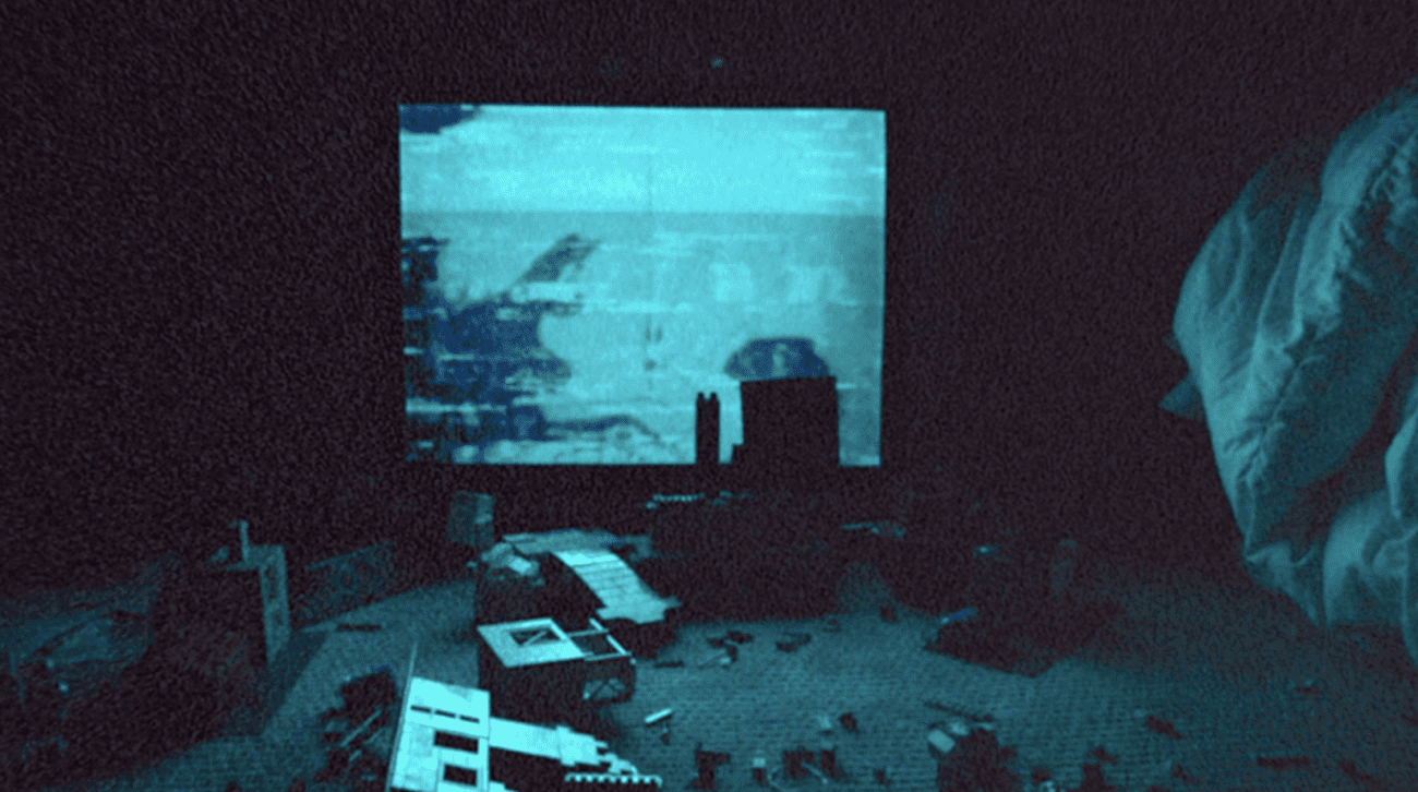 A grainy blue screen is shown in a dark, cluttered room.