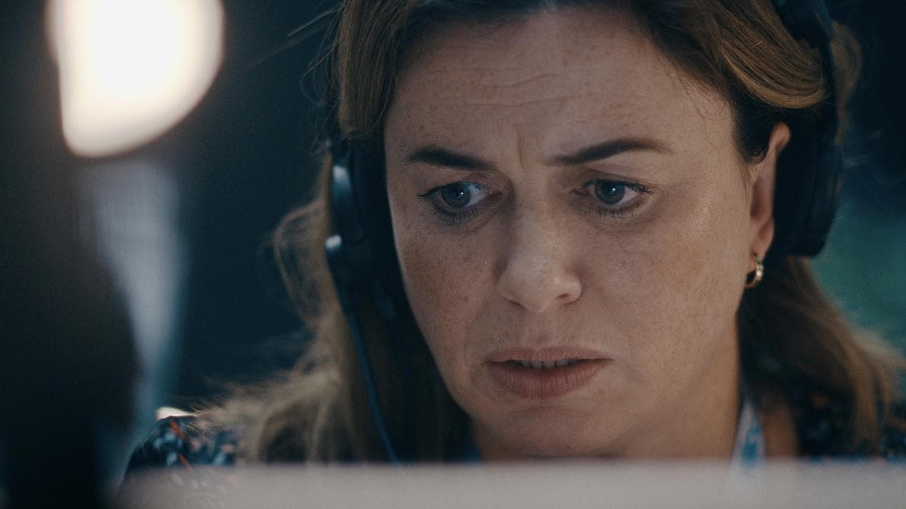 Μια γυναίκα με ακουστικά κοιτάζει μια οθόνη υπολογιστή προβληματισμένη.