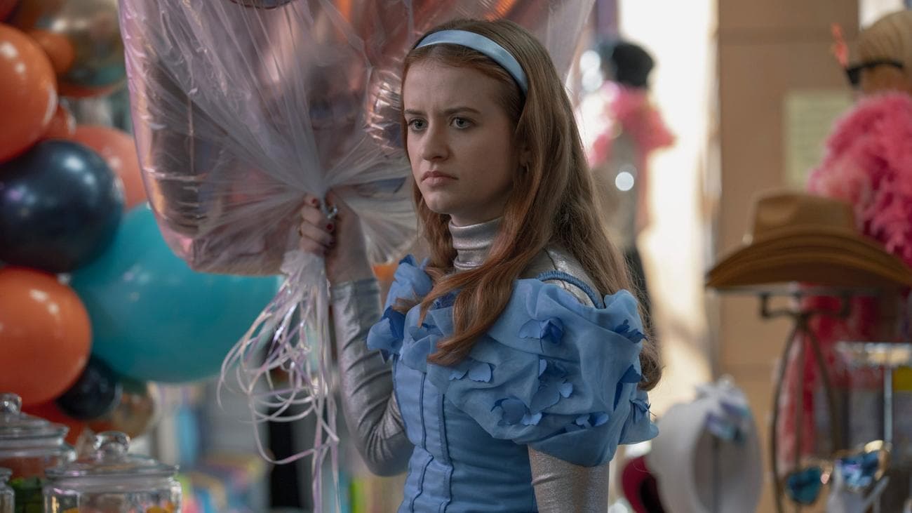 Máiréad Tyers is dressed in a pale blue gown and headband standing holding balloons in a costume shop.