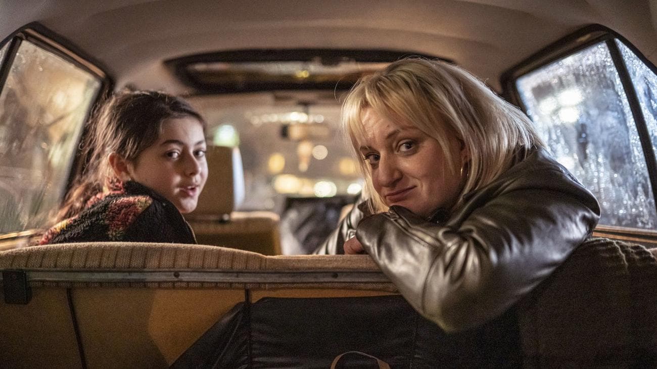 Fleur Tashjian and Daisy May Cooper sit in a car, turning to smile at the camera.