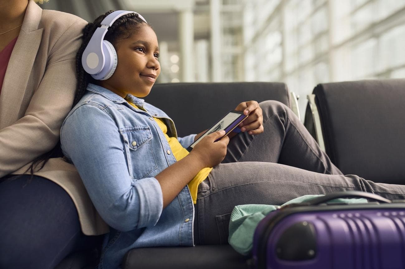 Άτομο που κάθεται σε ένα αεροδρόμιο φορώντας ακουστικά και διαβάζει σε ένα Kindle Kids Paperwhite