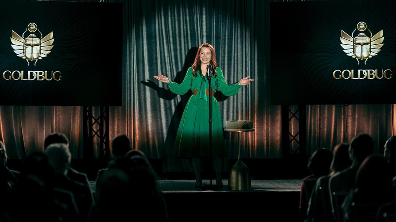 Μια γυναίκα με ένα πράσινο φόρεμα στέκεται στη σκηνή στο προσκήνιο.