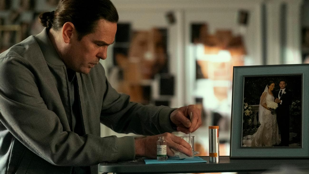 Ένας άντρας προσθέτει μια λευκή σκόνη σε ένα ποτήρι σε ένα τραπέζι δίπλα σε μια φωτογραφία γάμου.