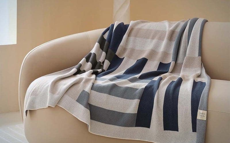A striped Double Stitch by Bedsure Throw Blanket draped over a cream-colored couch.