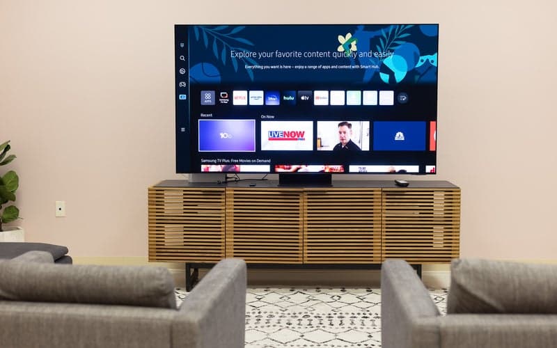 The Samsung S95C OLED on a stand in a room with two chairs