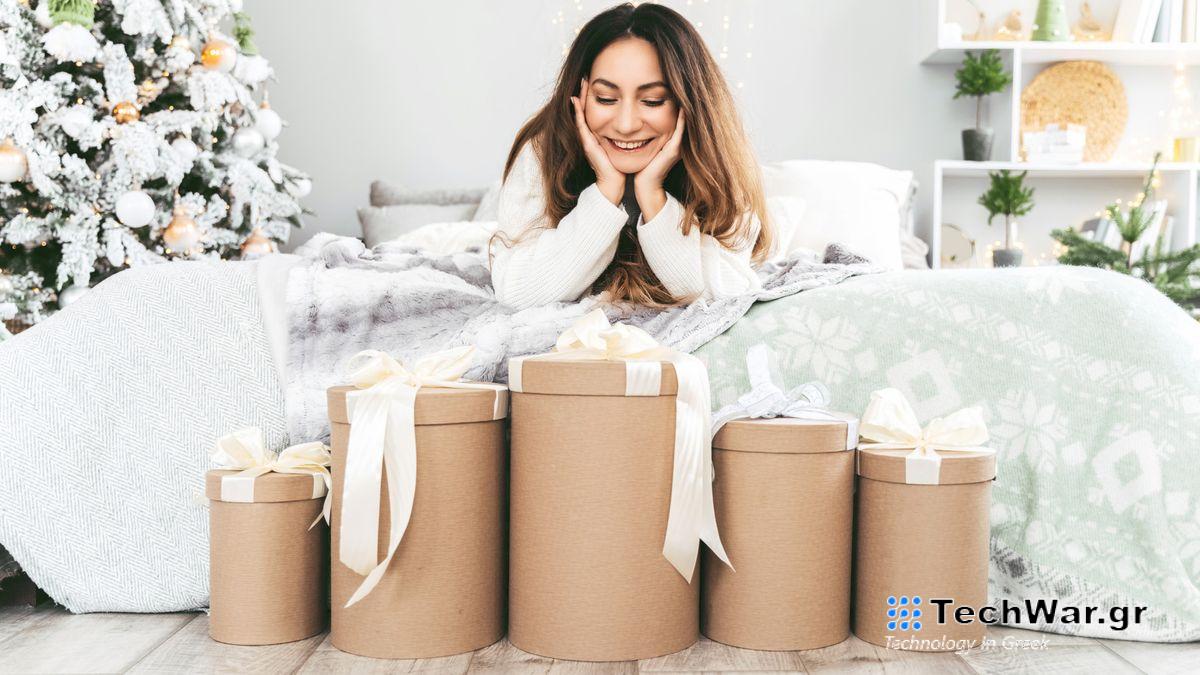 A woman with long dark hair lies on her stomach looking at a pile of beautifully wrapped Christmas gifts tied with white bows