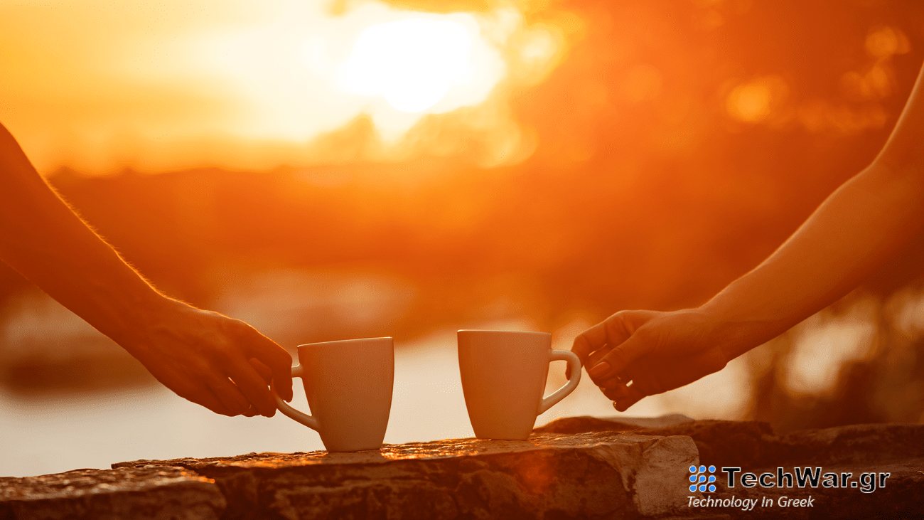 Two people hold coffee cups while looking at a a sunrise.