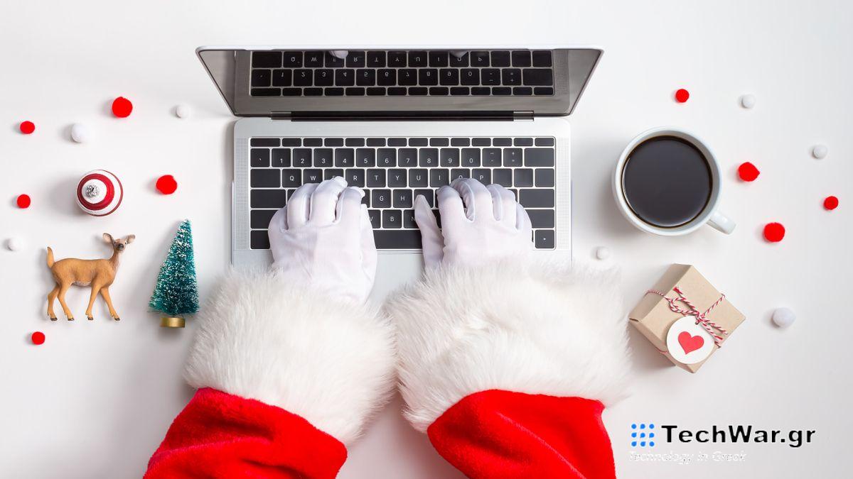 Santa hands in white gloves with red sleeves and white fluffy cuffs seen from above, typing on a laptop, surrounded by small Christmas ornaments