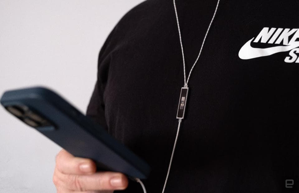 Ακουστικά Questyle NHB15 In-Ear Monitor συνδεδεμένα με ένα τηλέφωνο στο χέρι κάποιου.