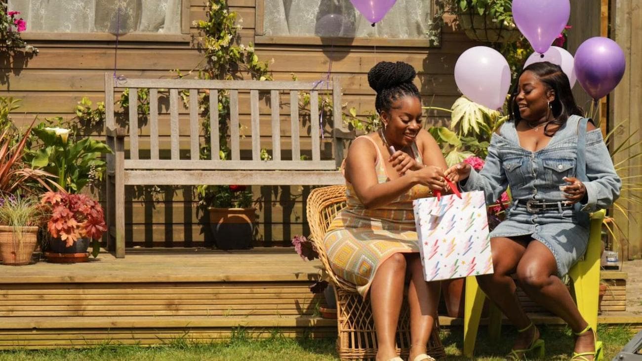 Two women sit opening presents in a back garden.