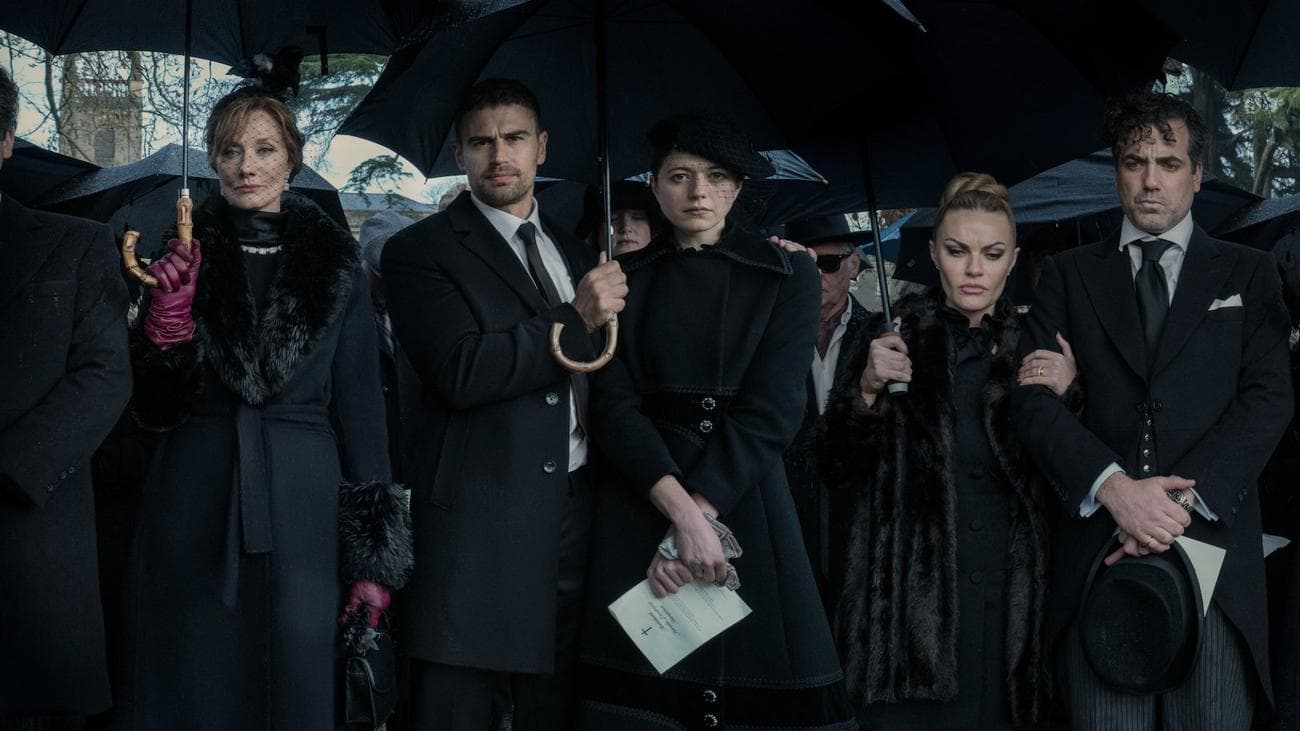 A group stand under umbrellas dressed in black at a funeral.