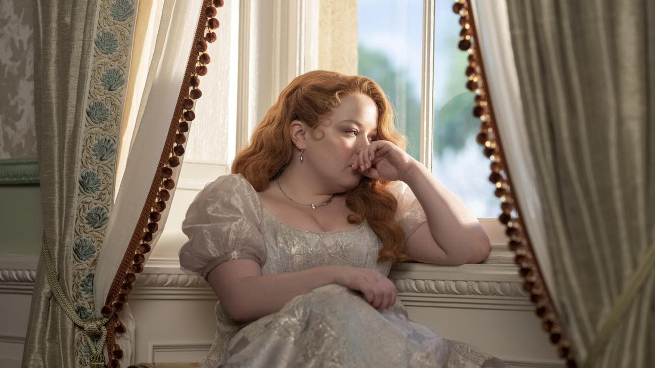 A woman in Regency costume sits in thought by a window.