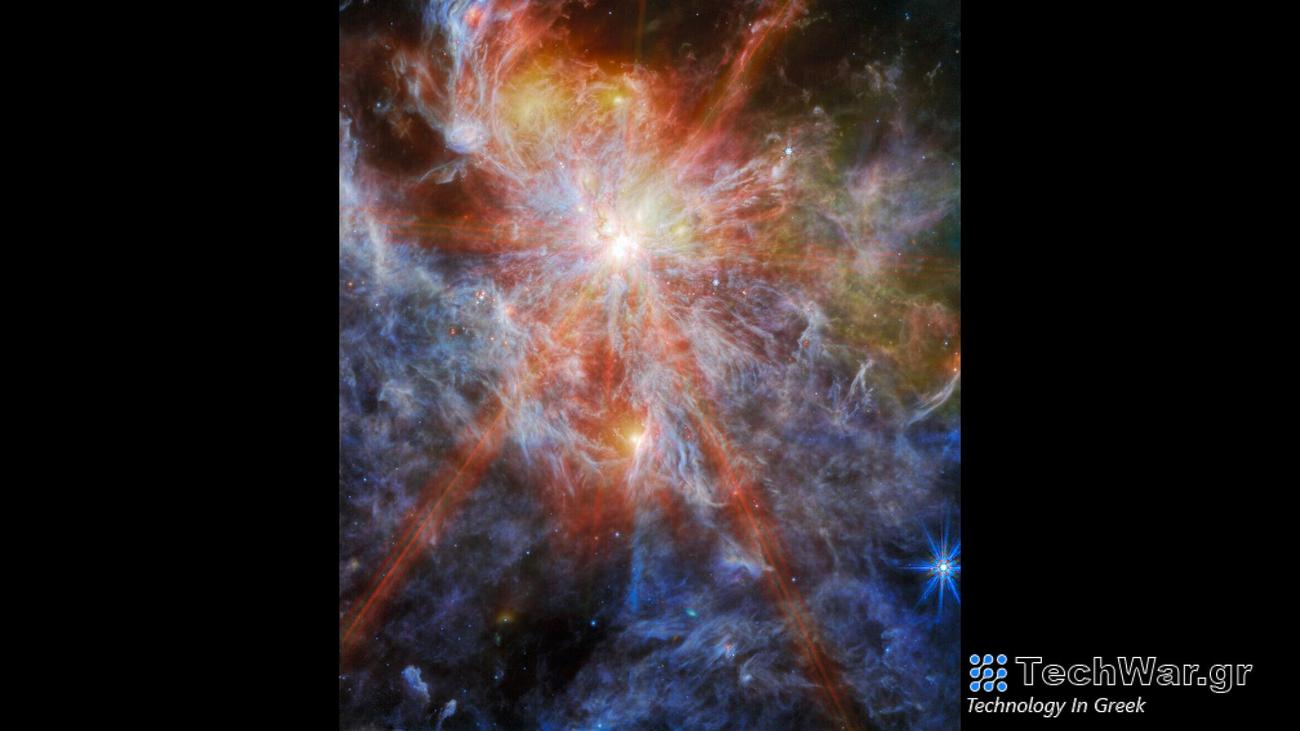 A bright young star within a colorful nebula. The star is identifiable as the brightest spot in the image, surrounded by six large spokes of light that cross the image. A number of other bright spots can also be seen in the clouds, which are shown in great detail as layers of colorful wisps.