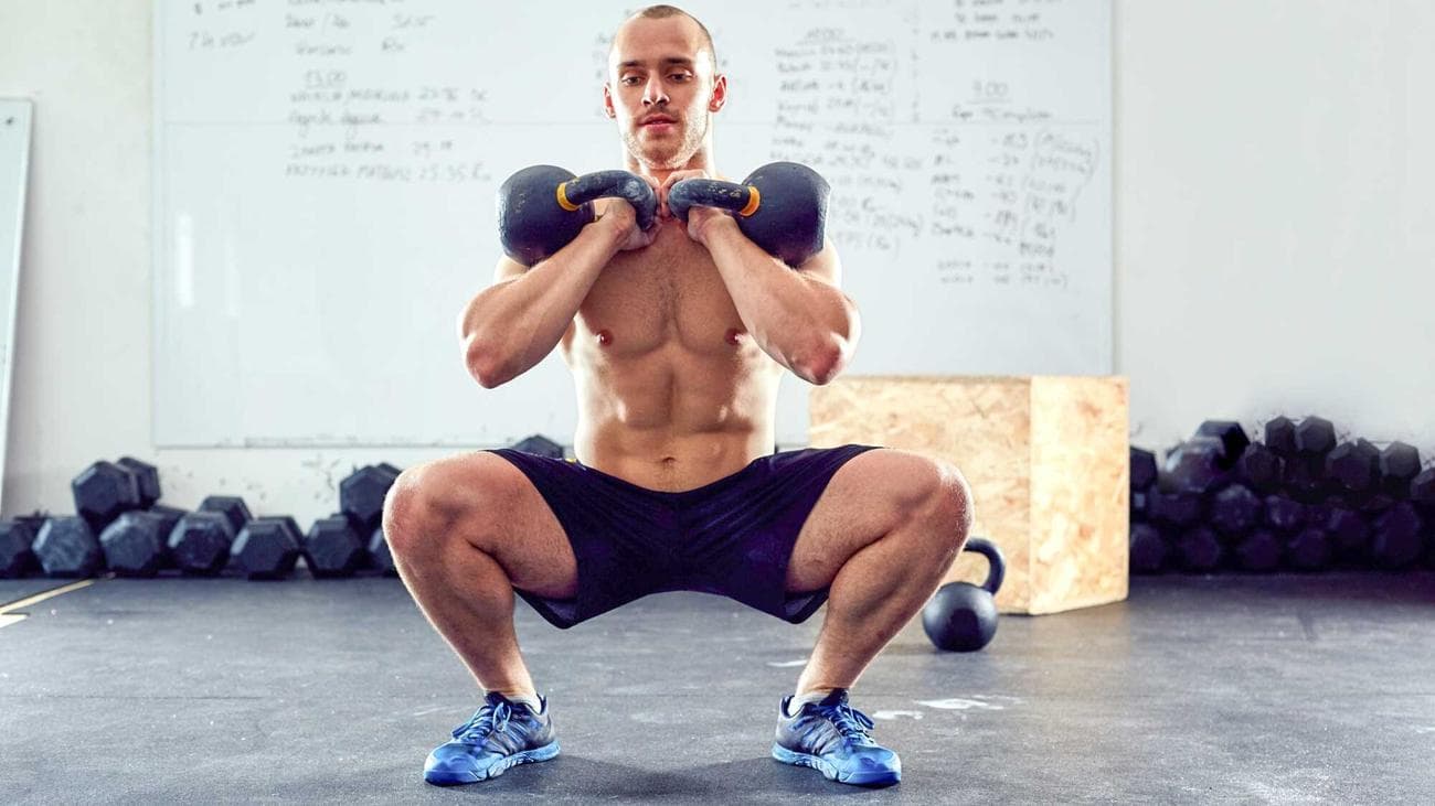 Άνδρας που εκτελεί ένα ωστήριο kettlebell με δύο kettlebells σε θέση οκλαδόν