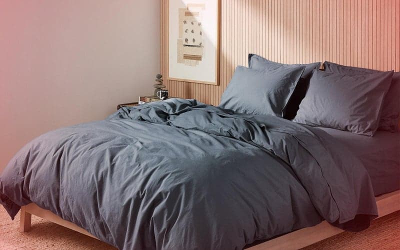 Βαμβακερά σεντόνια βουρτσισμένα με αλεξίπτωτο σε ένα κρεβάτι σε μπλε χρώμα σε ένα αραιό δωμάτιο