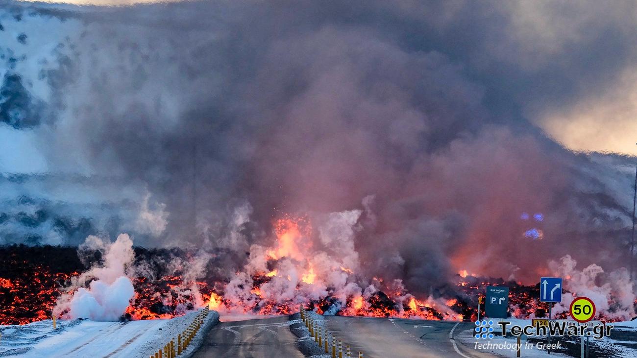Molten lava overflows the road leading to the Blue Lagoon geothermal spa, a popular tourist destination in western Iceland. Orange lava covers a dark road, as gray smoke rises.