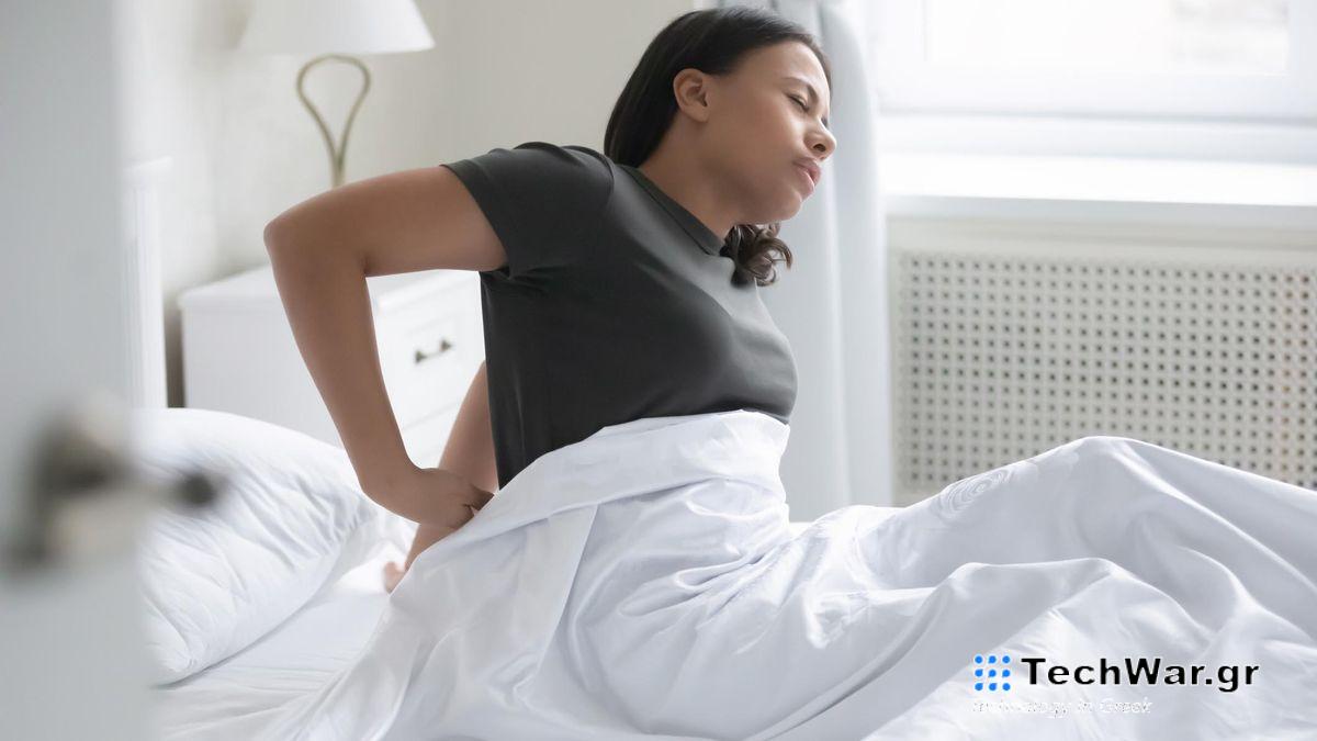 Hard vs soft mattress image shows a woman in a brown t-shirt massages her painful lower back in bed 