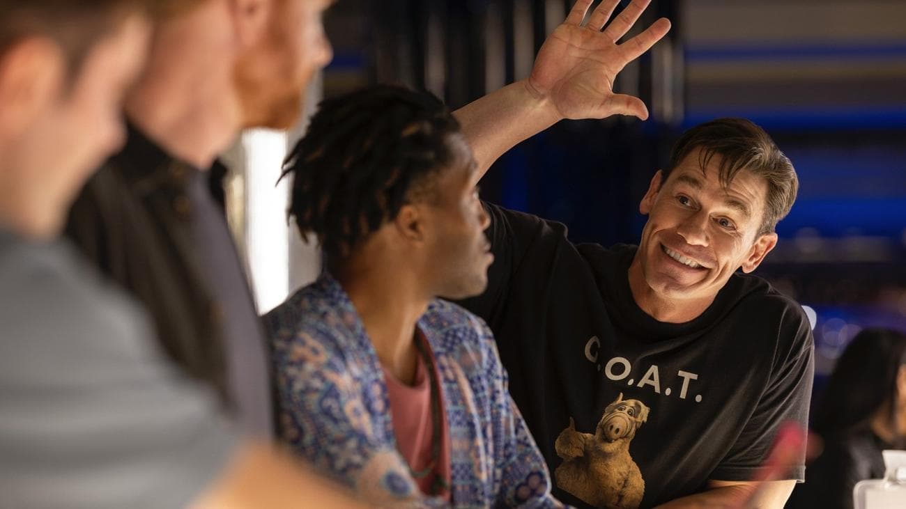 Ένας άντρας με πουκάμισο ALF κουνάει άλλους τρεις άντρες απέναντι από το μπαρ.