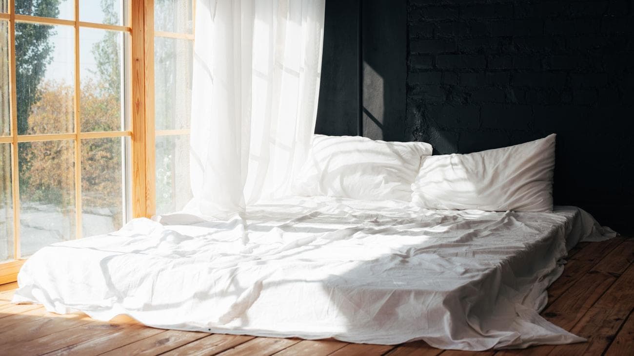 Ένα στρώμα φουτόν με λευκά κλινοσκεπάσματα μπροστά σε μια ανοιχτή χήρα