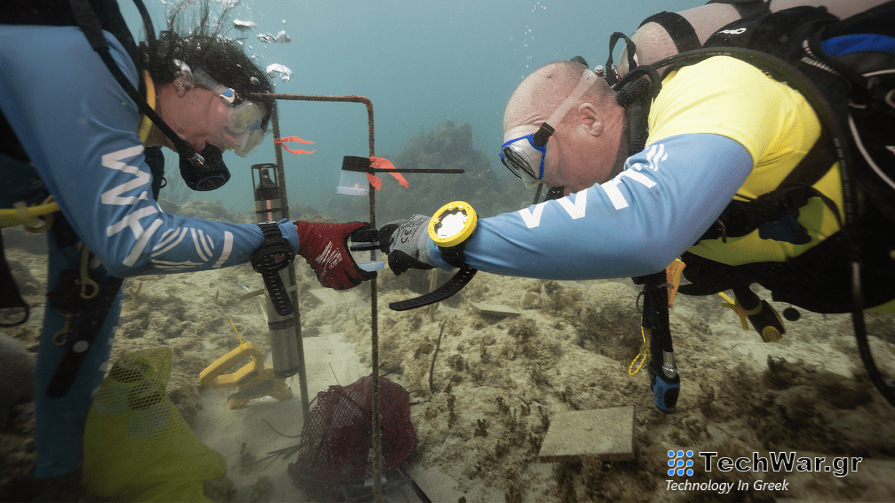 two men in scuba gear install a sound system by a coral reef