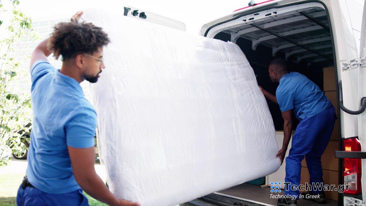 Two people place a covered mattress in a van to move it to a new house