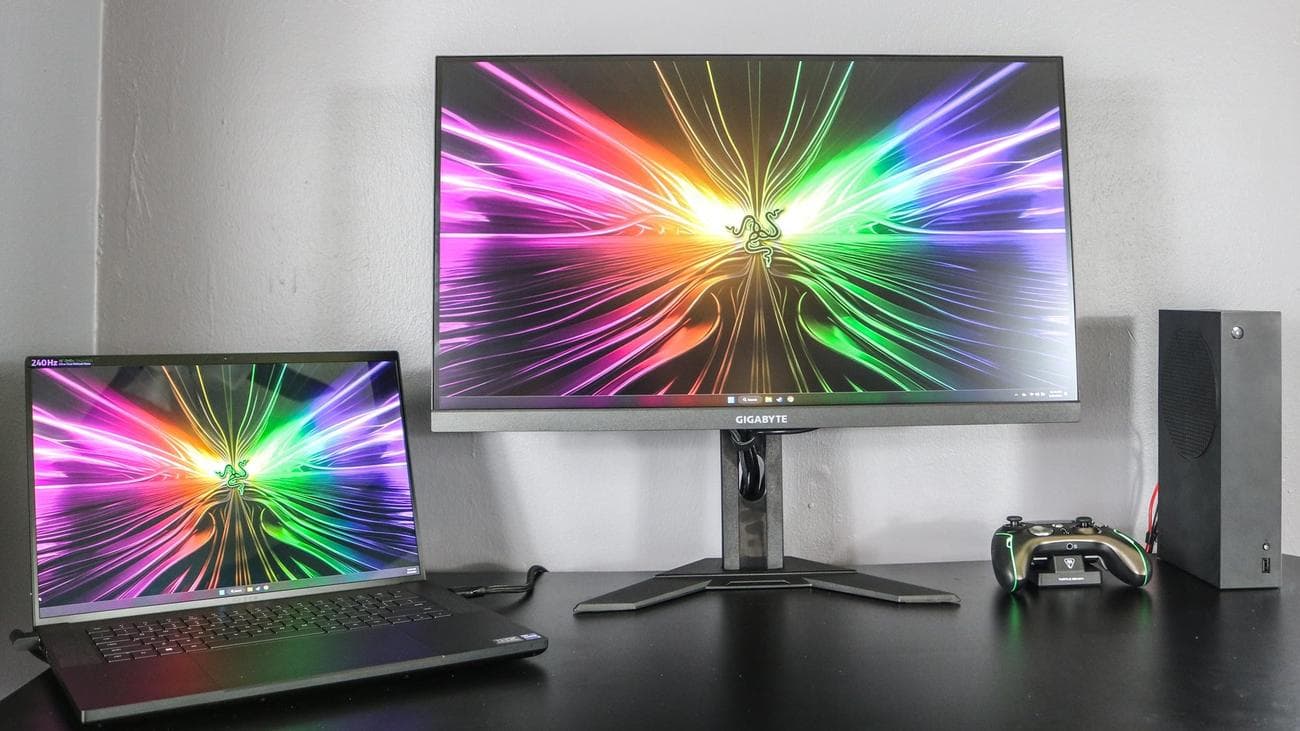 Η οθόνη παιχνιδιών Gigabyte M28U σε ένα γραφείο με Xbox και φορητό υπολογιστή παιχνιδιών