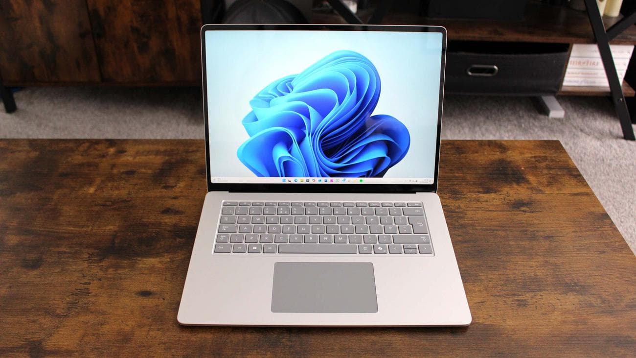 Surface Laptop 7 open on a wooden table with Windows 11 wallpaper on screen