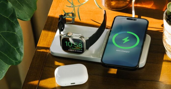 An iPhone and Apple Watch on a table charging on Nomad’s Base One Max wireless charger, with a set of AirPods near.