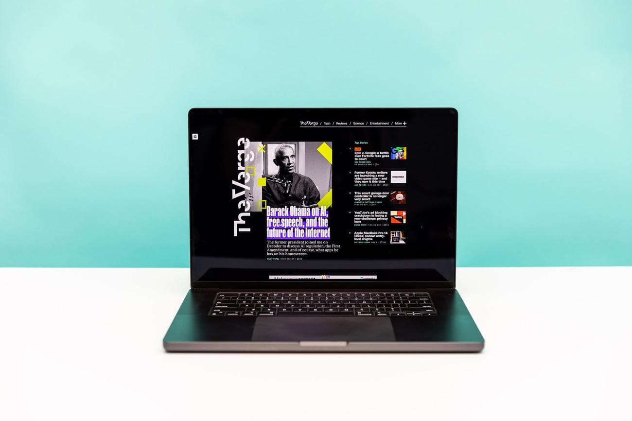 The M3 Max MacBook 16 in space black in front of a teal and white background.