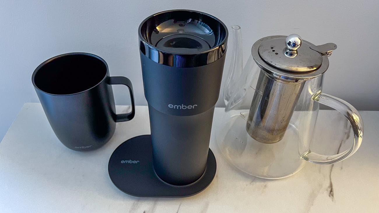 Ember Travel Mug 2+ στην πλάκα φόρτισης που κάθεται ανάμεσα στην Ember Mug 2 και έναν γυάλινο βραστήρα