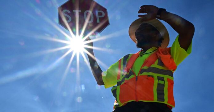 A person wearing an orange work vest holds up a stop sign. The sign shines brightly behind them.
