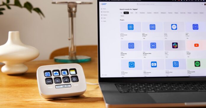 An Elgato Stream Deck Neo plugged into and sitting beside a laptop on a desk.